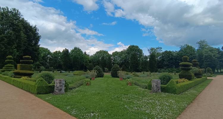 Jardin formel symétrique avec des haies taillées et des statues sous un ciel partiellement nuageux