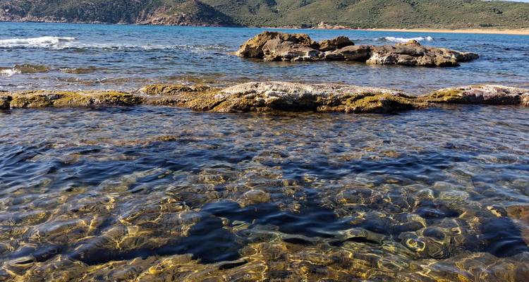 Crystal clear shallow sea water with rocky outcrops and distant green hills.