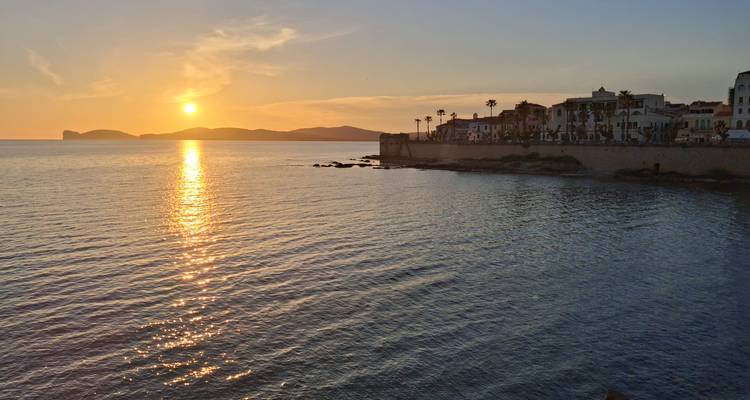 Golden sunset over the sea illuminating historic walled town and distant island silhouettes.