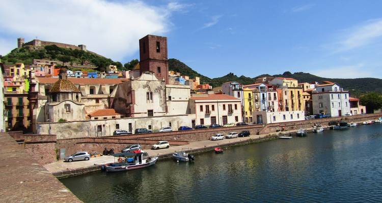 Riverside town with medieval castle and pastel buildings reflecting in calm water.