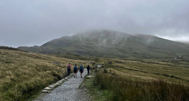 Small group of walkers on a gravel path toward a mist-shrouded mountain in Snowdonia.