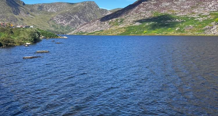 Blue lake surrounded by steep, green Welsh mountains under a clear sky.
