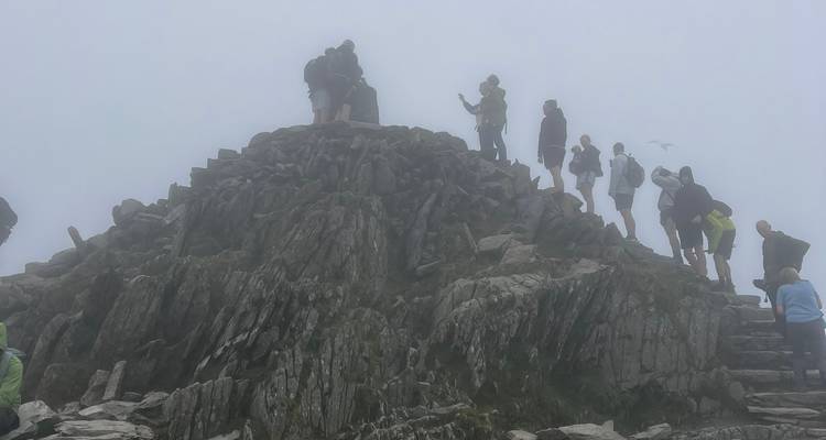 Crowd of climbers standing on a rocky peak enveloped in dense fog.