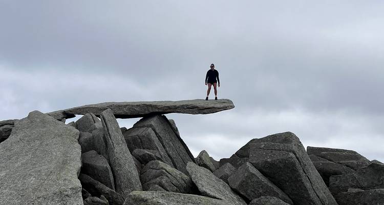 Adventurer standing triumphantly on the dramatic cantilever stone against a grey sky.