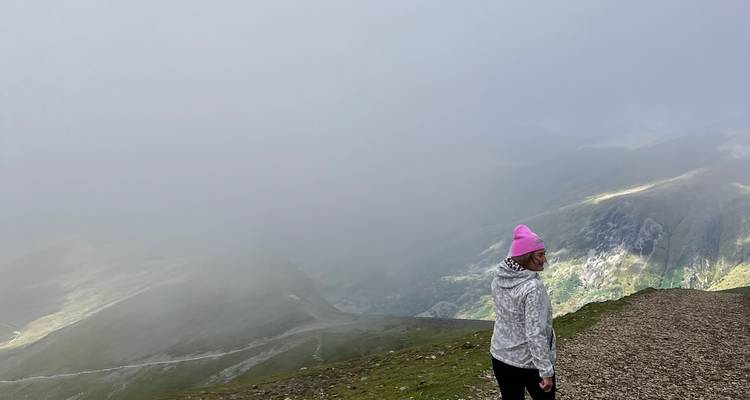 Hiker in pink beanie looking back along a fog-covered mountain trail.