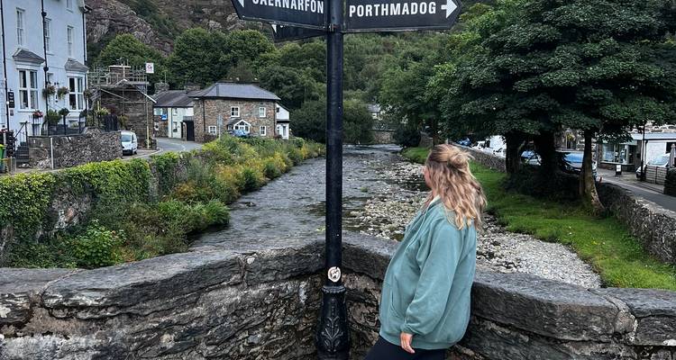 Traveler standing at a crossroads signpost beside a river in a quaint Welsh village.