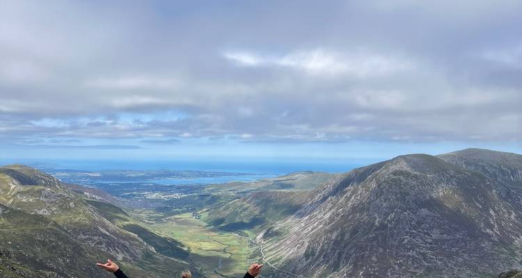 Hikers celebrating on a high Snowdonia ridge with expansive coastal views below.