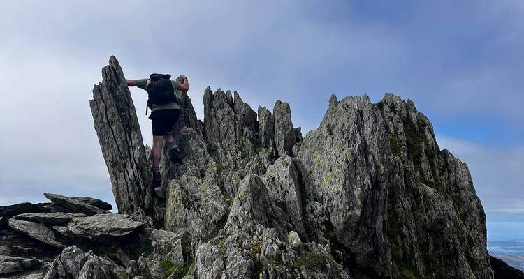 Climber scrambling up jagged rock pinnacles under a bright but hazy sky.
