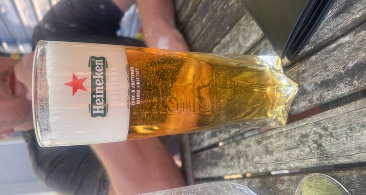 Chilled pint of Heineken beer on an outdoor wooden table on a sunny day.