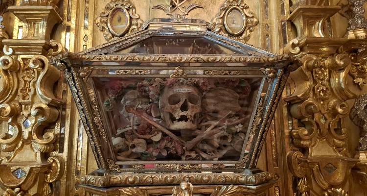 Prunkvolles goldenes Reliquiar mit einem menschlichen Schädel und Knochen in einem aufwändig dekorierten Kircheninneren.
