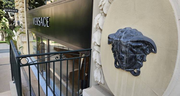 Elegant storefront of Versace with a sculpted Medusa fountain plaque and wrought-iron railing.