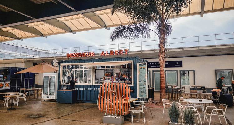 Trendy container food kiosk "Monsieur Albert" with outdoor seating and a tall palm in an airy market space.
