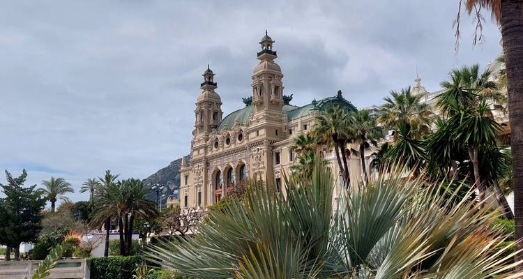 Elegant façade of the Monte Carlo Casino crowned with twin towers, framed by palm trees and exotic plants.