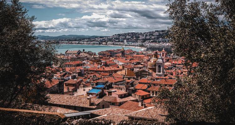 Framed vista of Nice old town roofs and coastline seen through foliage and trees.