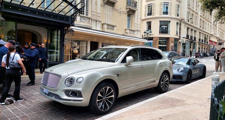 Bentley SUV and Porsche sports car lined up outside a luxury Monaco hotel with valet staff nearby.