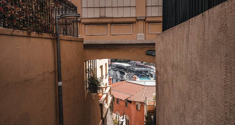 Narrow passageway between ochre walls revealing a glimpse of Monaco harbour below.