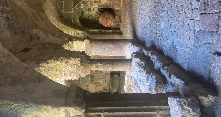 Intérieur en pierre ancienne avec colonnes, arcs et sol inégal éclairé par une lumière naturelle douce.