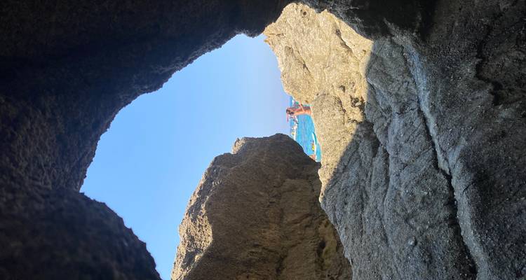 Personne vue à travers une ouverture rocheuse, se prélassant au soleil sur des rochers côtiers à côté d'une mer d'un bleu éclatant.