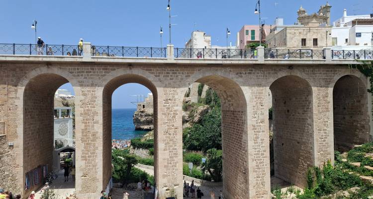 Steinbrücke mit mehreren Bögen überquert eine Schlucht, die zum Meer führt, mit der Stadt und Besuchern oben.