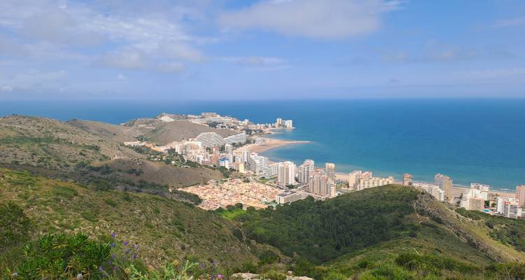 Vue en plongée d'une ville côtière et d'une mer turquoise encadrées par des collines verdoyantes.