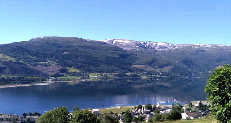 Lac tranquille reflétant les montagnes avec des plaques de neige et un ciel bleu clair au-dessus d'une petite ville.