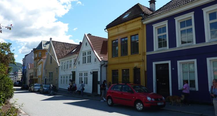 Rue de maisons de ville en bois coloré avec des voitures garées et des piétons profitant d'une journée ensoleillée.