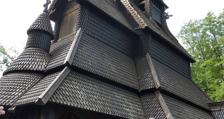 Extérieur complet d'une église en bois à colombages de couleur sombre avec des motifs de bardeaux complexes située parmi de grands arbres.