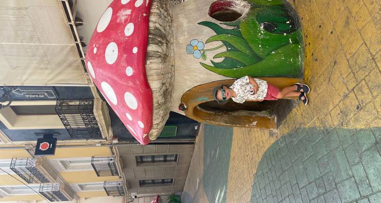 Un enfant pose à l'intérieur d'une sculpture géante de champignon fantaisiste sur une rue colorée