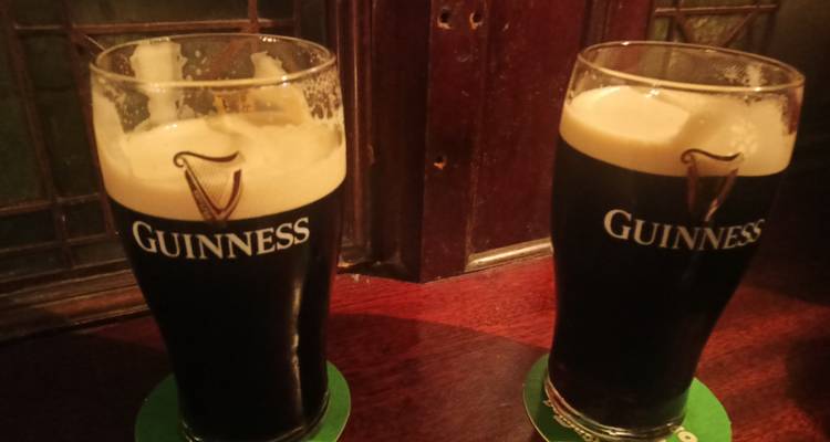 Deux pintes de Guinness fraîchement versées sur une table de pub en bois.