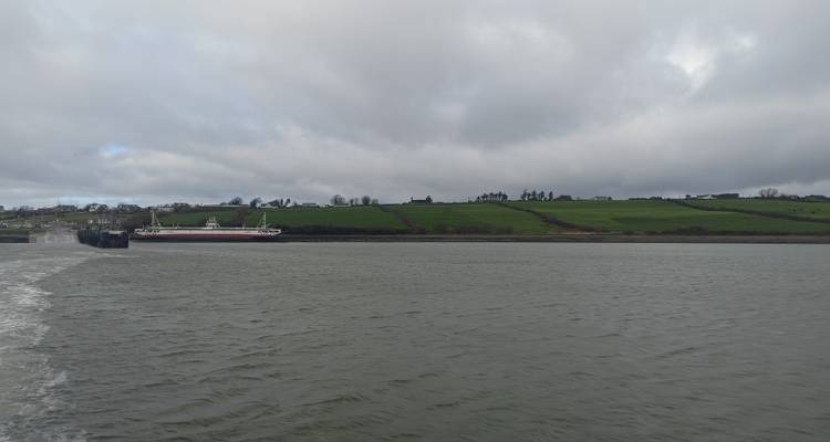 Les terres agricoles verdoyantes et basses ainsi qu'un bateau-passeur aperçus depuis le sillage arrière par une journée grise.