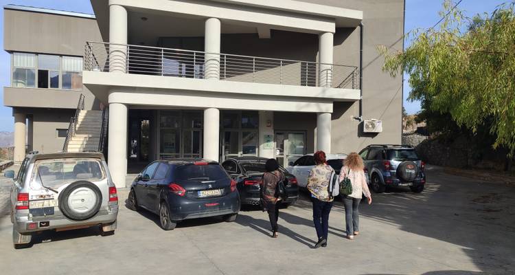 Three women walk toward a modern municipal building with parked cars in front.