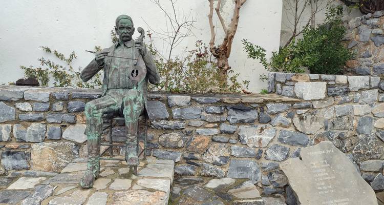 Bronze statue of a seated musician playing a traditional lyra against a stone wall backdrop.