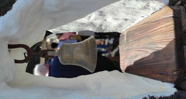 Petite cloche en laiton suspendue dans une niche blanchie à la chaux avec une file de visiteurs flous en arrière-plan.