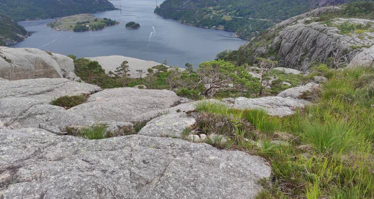 Sommet rocheux dominant une étroite vallée glaciaire avec une petite île boisée et le sillage d'un bateau.