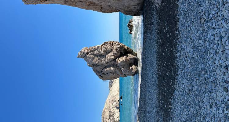 Iconic sea stack rising from turquoise waters beside a pebble beach