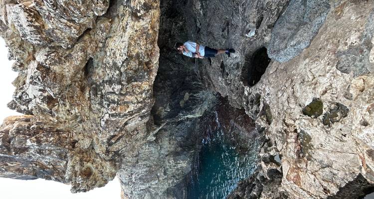 Traveler standing beneath a massive sea cliff overlooking deep blue water
