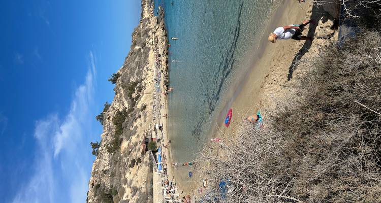 Small sheltered sandy cove with swimmers and sunbathers surrounded by rocky hills
