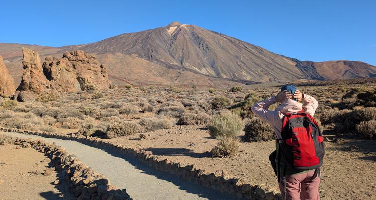 Randonneur avec un sac à dos rouge admirant le cône volcanique du Mont Teide par une belle matinée claire.