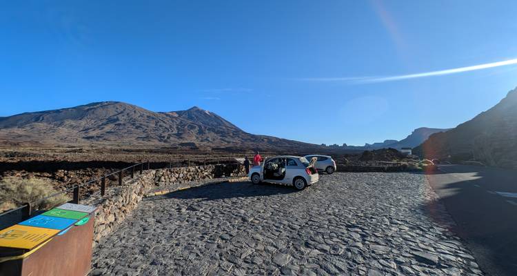 De petites voitures électriques garées sur un belvédère pavé avec un paysage volcanique aride en arrière-plan.