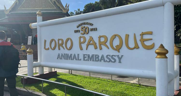 Grand panneau blanc pour l'Ambassade des Animaux de Loro Parque marquant le 50e anniversaire, avec un visiteur à proximité.