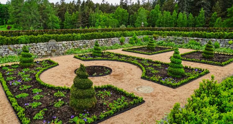 Symmetrical formal garden with clipped topiary and gravel paths inside stone walls.