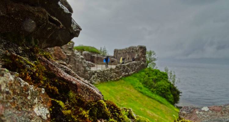 View of castle ramparts and loch through mossy rocks on a rainy day.