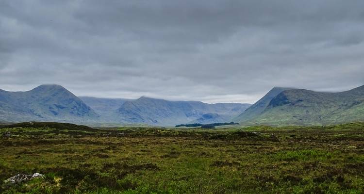Moody Highland moorland with distant mist-capped mountains under a blanket of clouds.