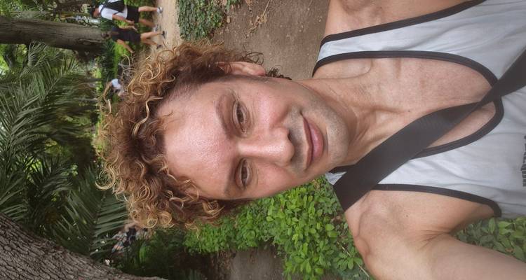 Sweaty selfie of a man in a tropical park with lush greenery behind