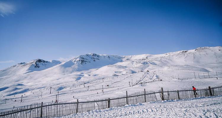 Vue panoramique d'une station de ski de montagne enneigée avec un ciel bleu dégagé et des pylônes de remontée mécanique.
