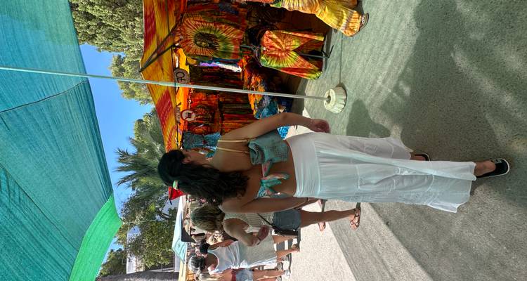 Marché hippie extérieur animé avec des étals colorés de tie-dye et des acheteurs.