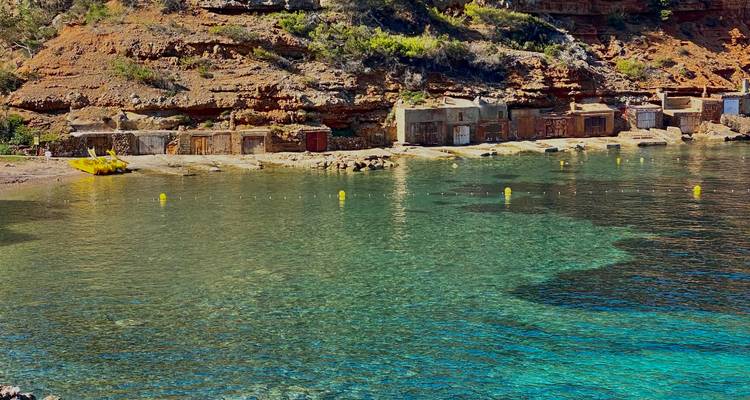 Une crique sereine avec des cabanes de pêcheurs traditionnelles bordant le rivage rocheux et l'eau émeraude cristalline.