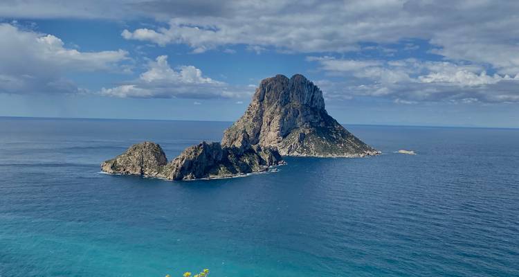 L'île d'Es Vedra se dresse devant une mer d'un bleu profond et un ciel parsemé de nuages.