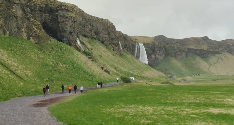 Long gravel path leading toward Seljalandsfoss waterfall framed by green cliffs.