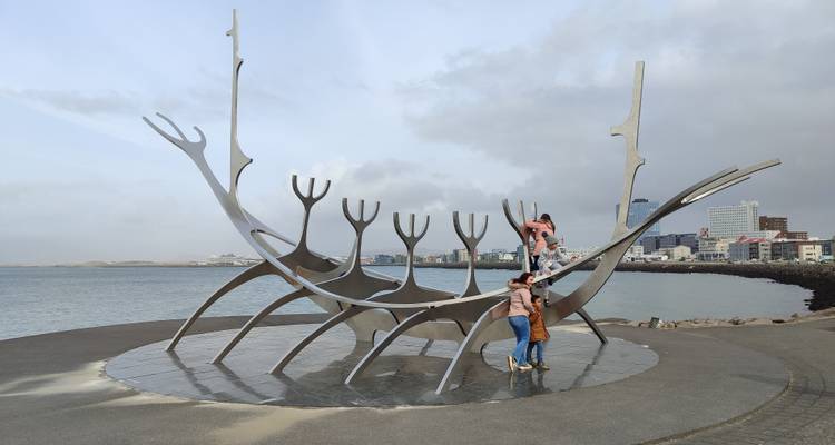 Children climb on the Sun Voyager sculpture beside Reykjavik’s waterfront with city skyline behind.